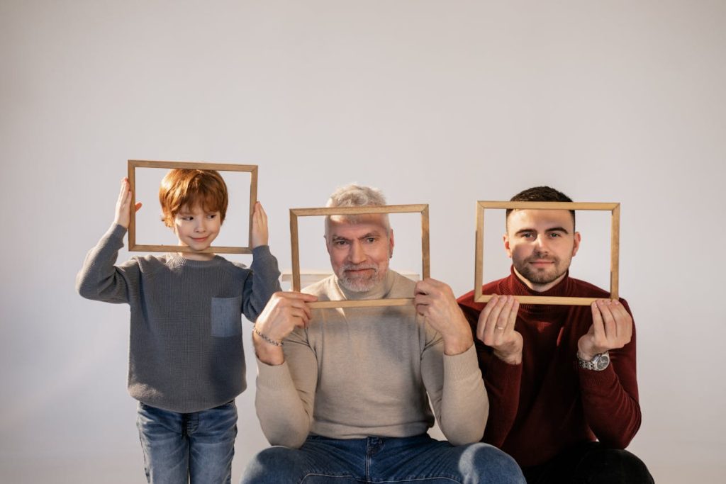 Two adult men with an age difference and a child, who appear to be one family. Each person's face is smiling through an empty picture frame that each one is holding.