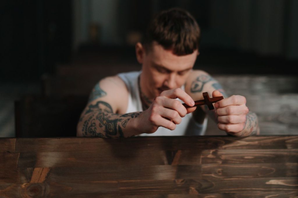 A tattooed young man with a cross is praying after conversion therapy
