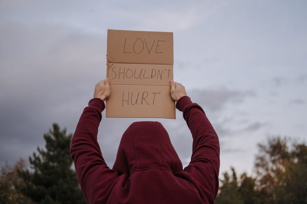 A campaigner against gay domestic violence wearing a red hoodie and holding a sign saying Love Shouldn't Hurt