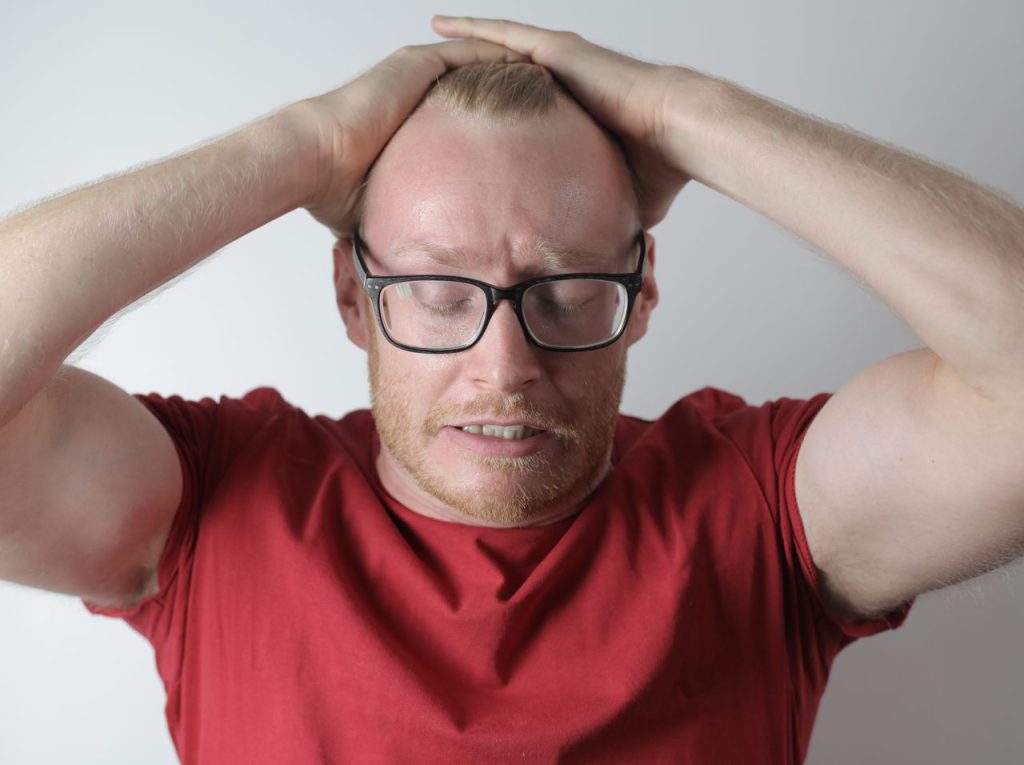 A frustrated man in a red shirt looking exasperated: the red flags for gay domestic violence include signs that are often missed